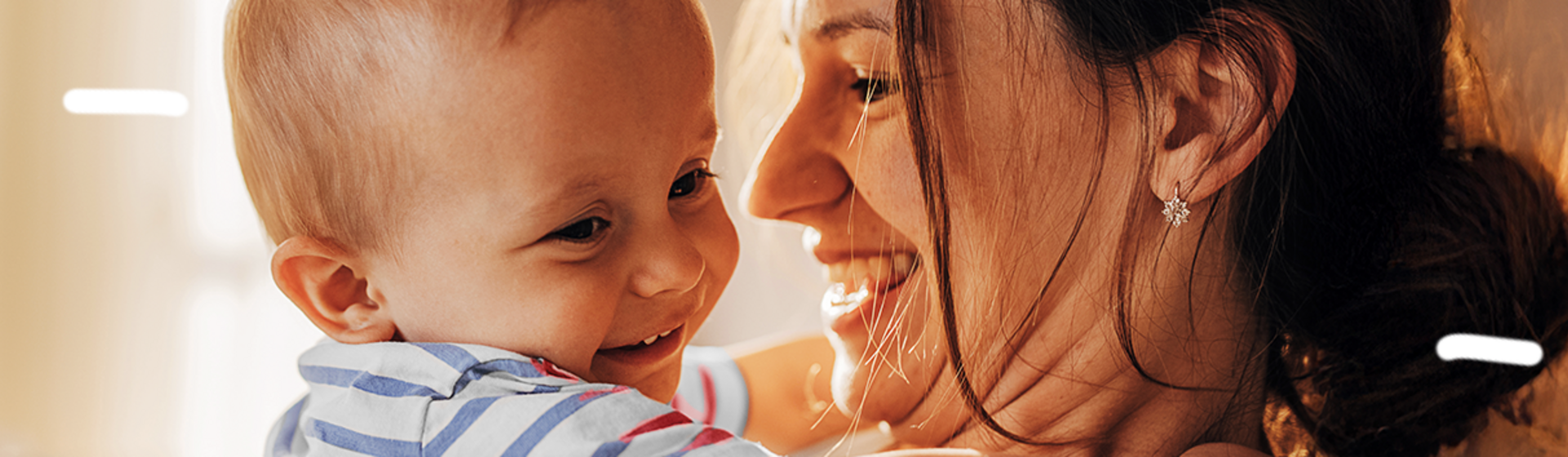Foto av en smilende mor som holder en lattermild baby i et varmt, solfylt rom